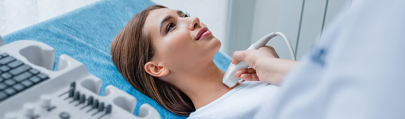 Ärztin untersucht den Hals einer Patientin mit einem Ultraschallgerät zur Kontrolle der Schilddrüse.